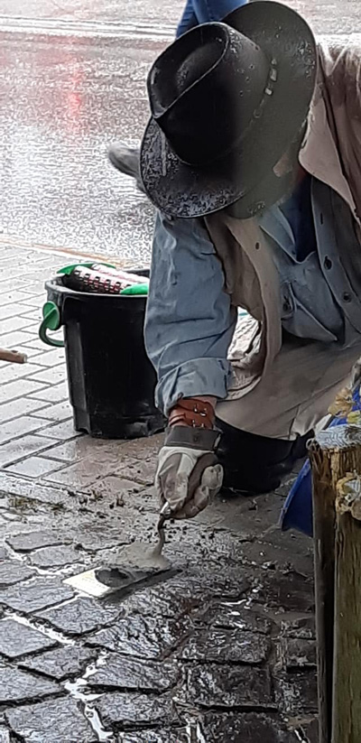 Gunter Demnig auf nasser Straße knieend beim Verlegen des Stolpersteins