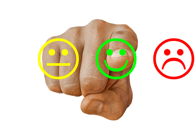 Eine Hand vor drei Smileys. In der Mitte ist ein grüner, der lächelt, links ist ein gelber, der einen  unzufriedenen 
 Strichmund macht und rechts ein roter, der verärgert ist. Der Zeigefinger der Hand zeigt auf den grünen, der fröhlich ist.